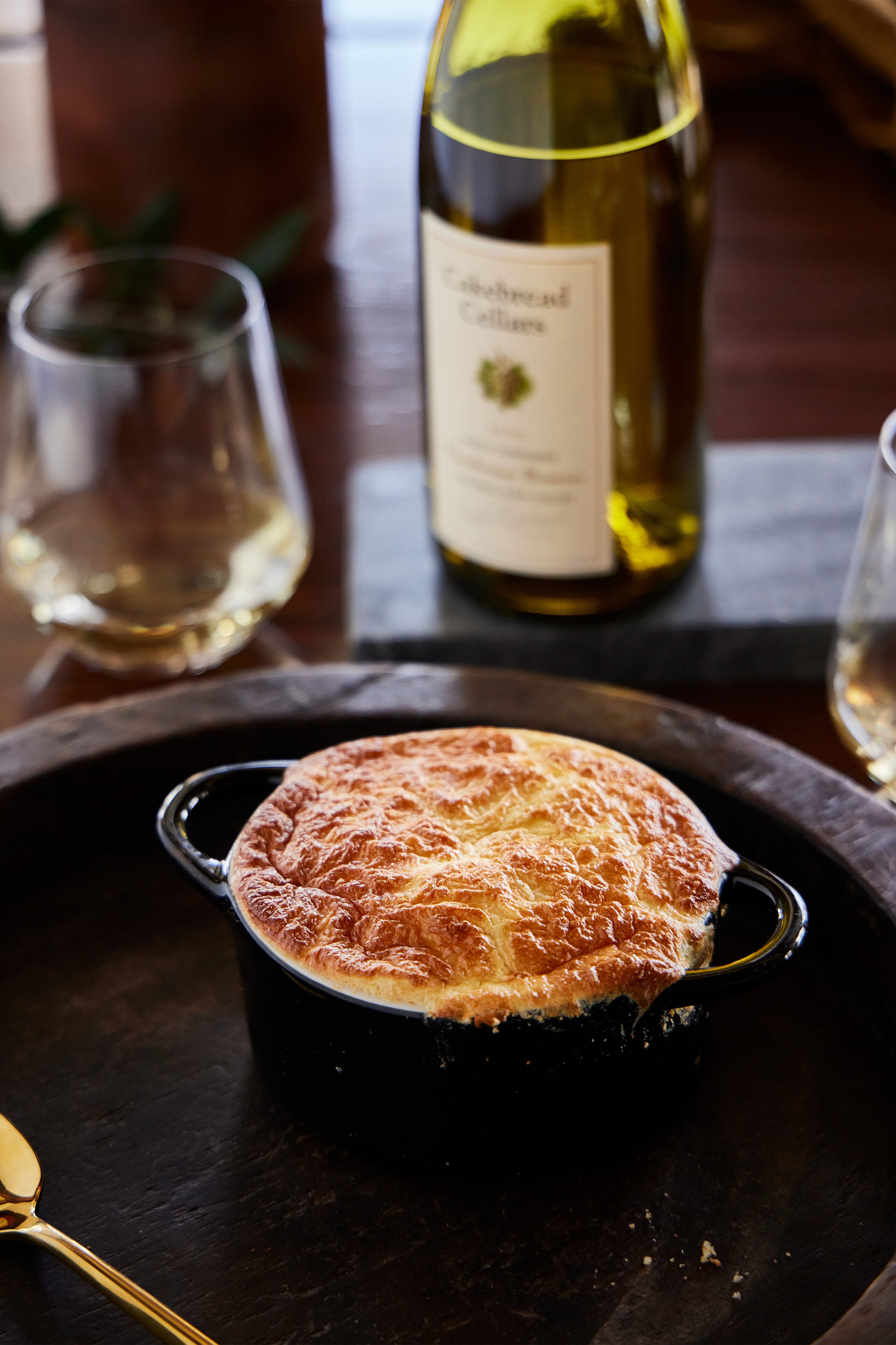 A delicious French Onion Soup with a golden, bubbly Gruyere cheese souffle on top served in a small black cast iron dish.