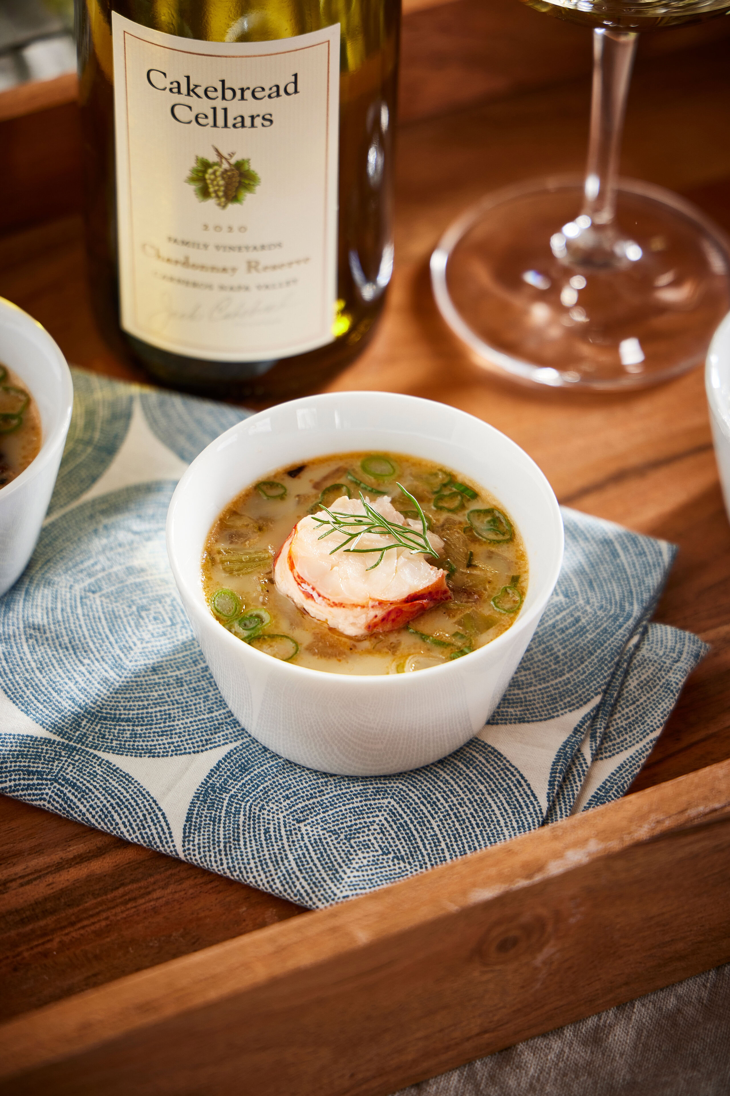 Creamy lobster Chawan Mushi with green onions and fresh herbs in a white bowl, served on a wooden tray with a glass of wine i.