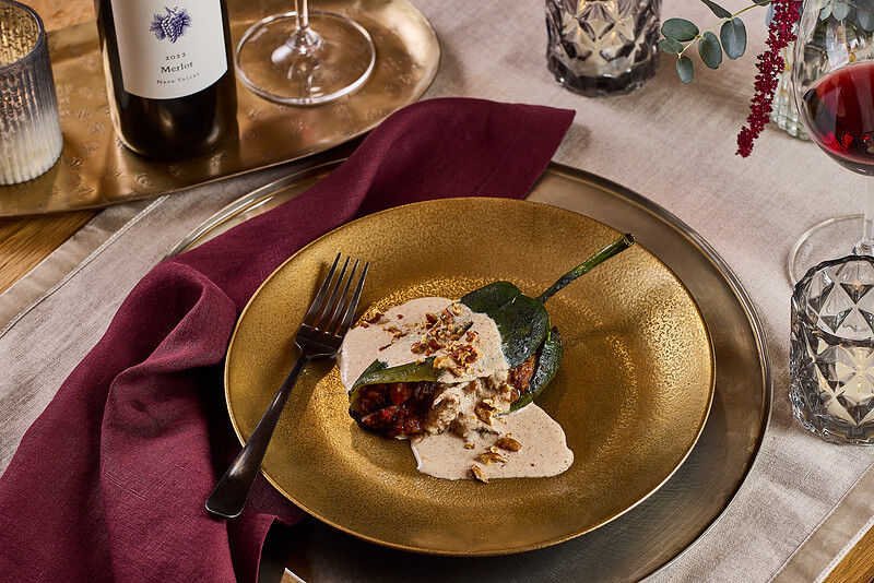 A delicious stuffed pasilla chile with walnut sauce served on a gold plate, accompanied by wine and elegant table setting.