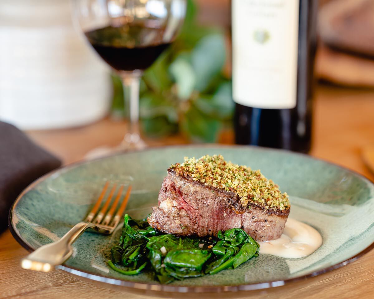 Grilled filet mignon with Andouille crust, served with garlic sauce and sautéed greens on a green ceramic plate.