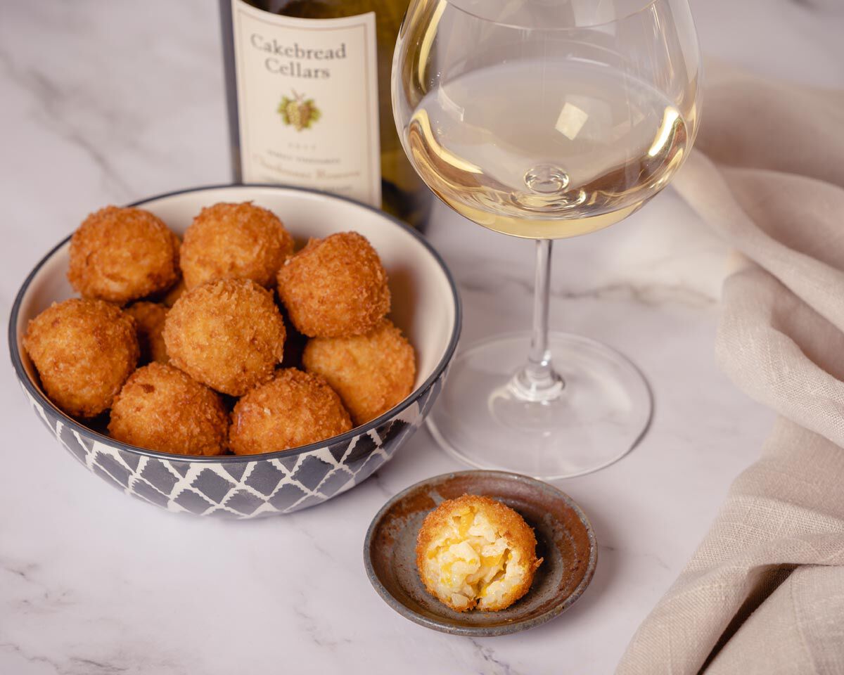 Crispy arancini with butternut squash and taleggio cheese served in a decorative bowl, with a glass of white wine and a bottl.
