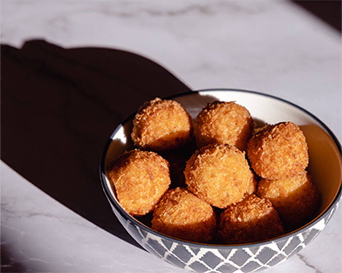 Golden arancini with fennel, Meyer lemon, and Crescenza cheese in a decorative bowl on a marble surface.