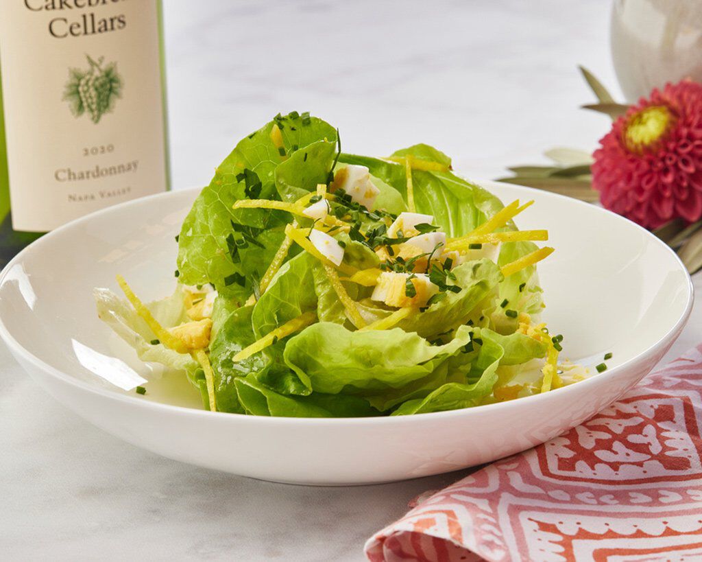 Fresh butter lettuce salad with Meyer lemon and herb vinaigrette in a white bowl, garnished with chopped herbs and lemon zest.