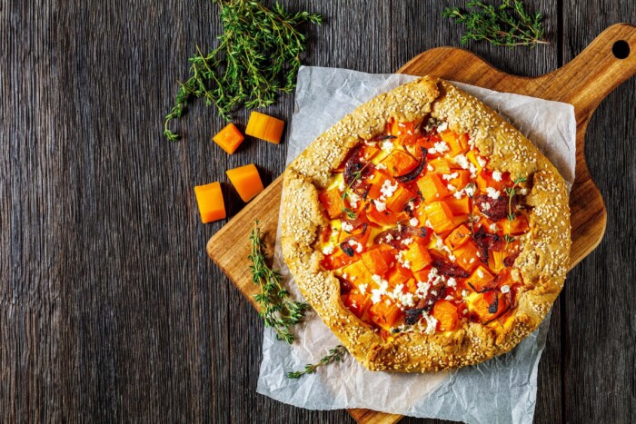 Creamy butternut squash, onion confit, and melted Gruyère cheese galette on a rustic wooden board with fresh herbs and diced.