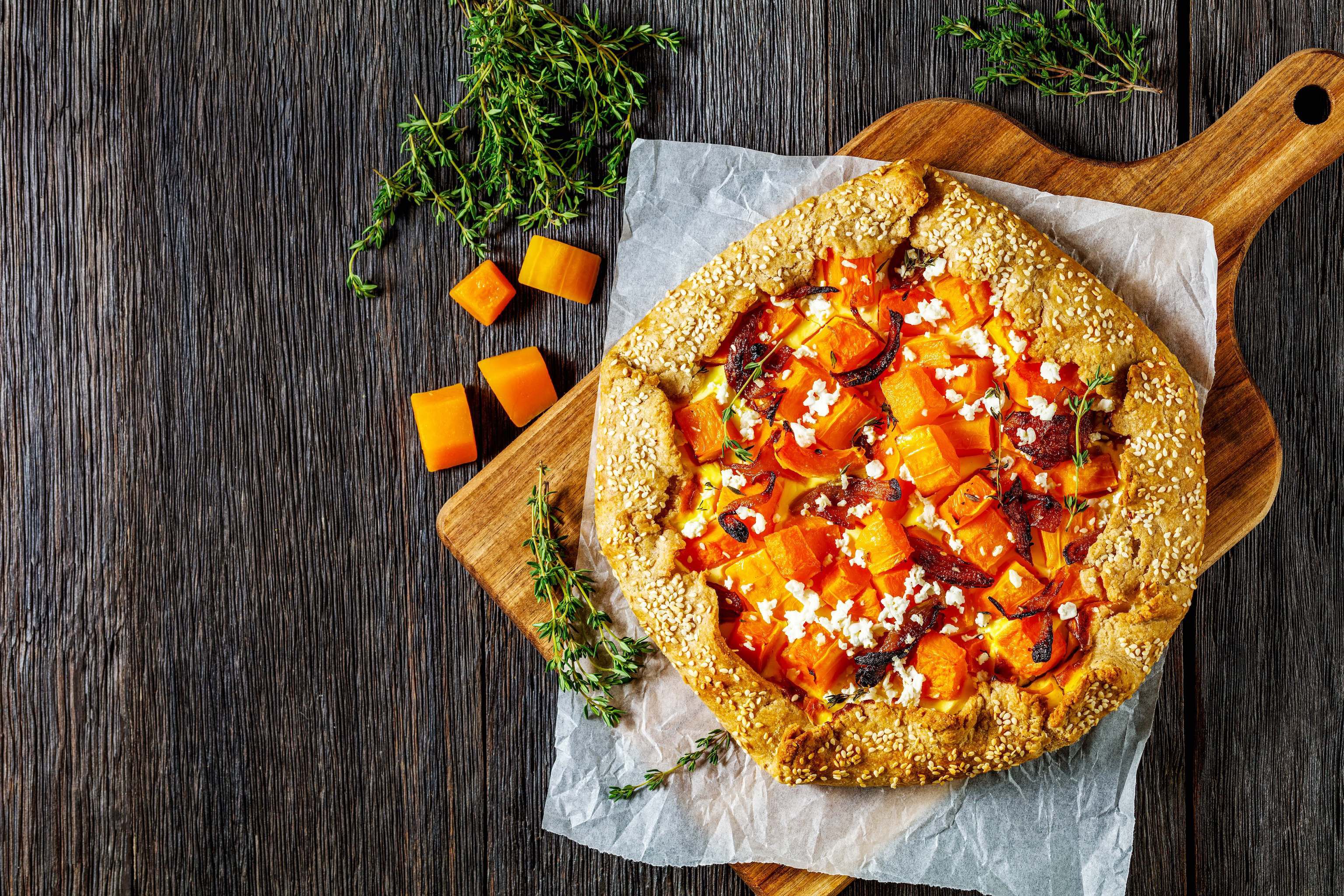 Creamy butternut squash, onion confit, and melted Gruyère cheese galette on a rustic wooden board with fresh herbs and diced.