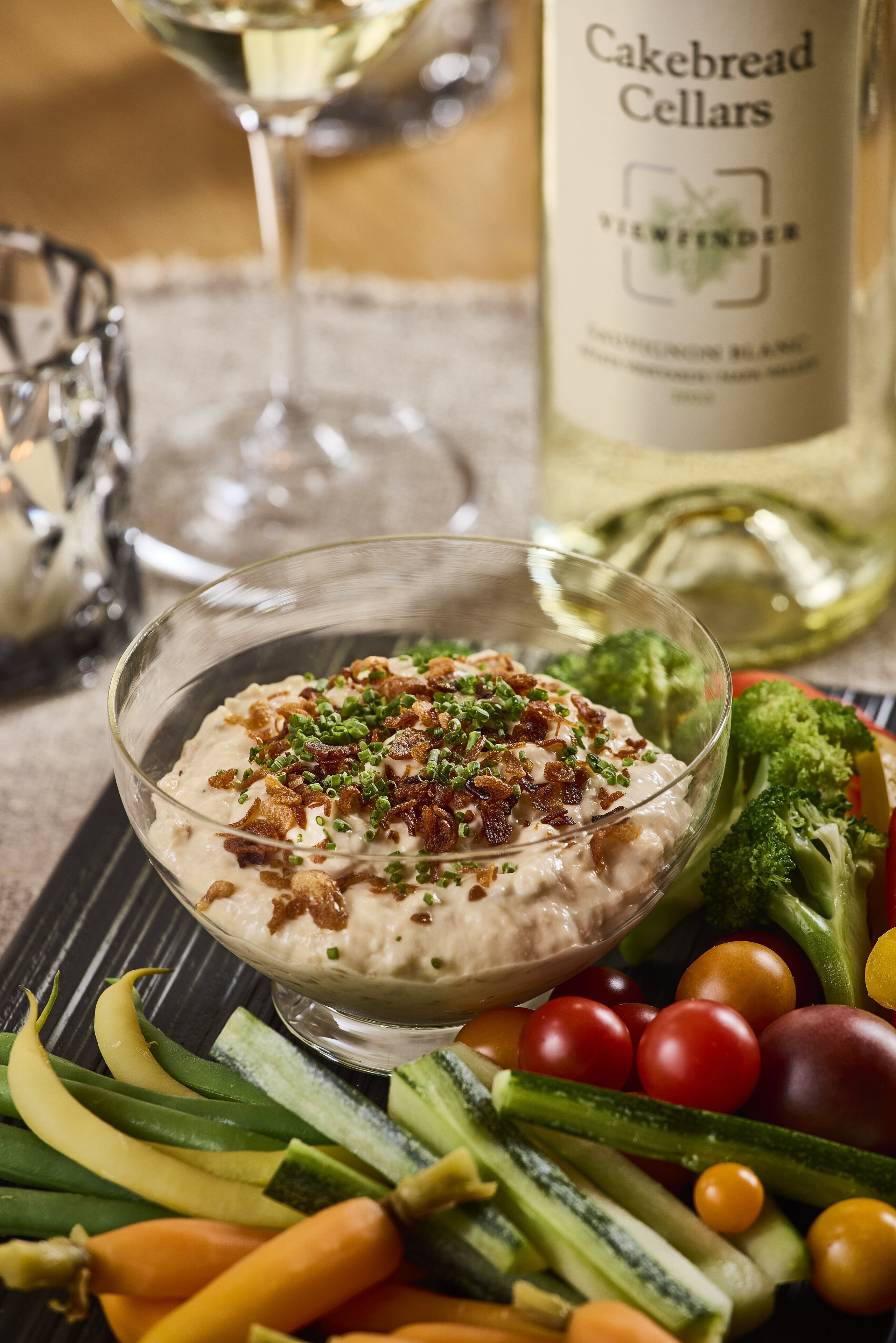 Creamy onion dip with chopped green onions served with fresh vegetables and a bottle of Cakebread Cellars wine in the backgro.