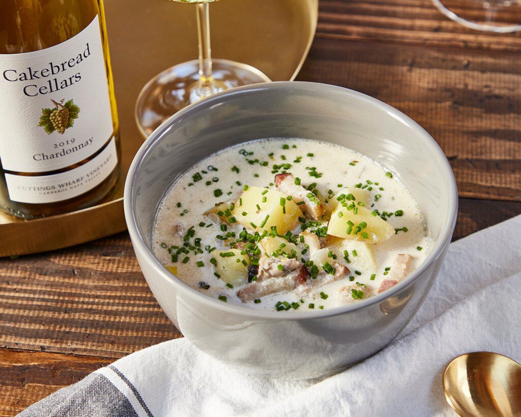 Creamy New England Clam Chowder with potatoes, leeks, and smoked bacon in a white bowl on a rustic wooden table.
