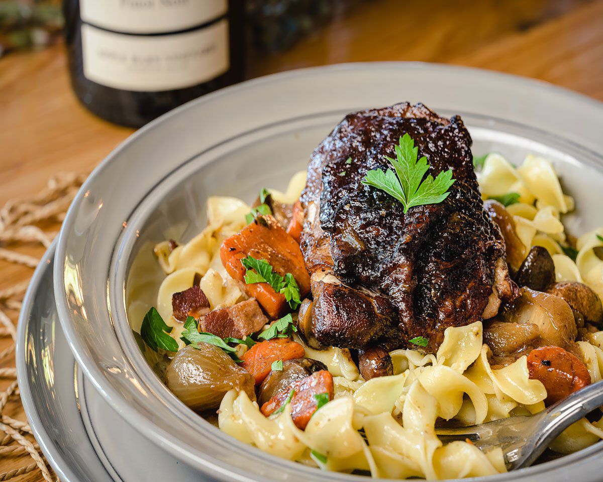 Succulent coq au vin with tender chicken, mushrooms, carrots, and herbs served over pasta, garnished with fresh parsley, on a.