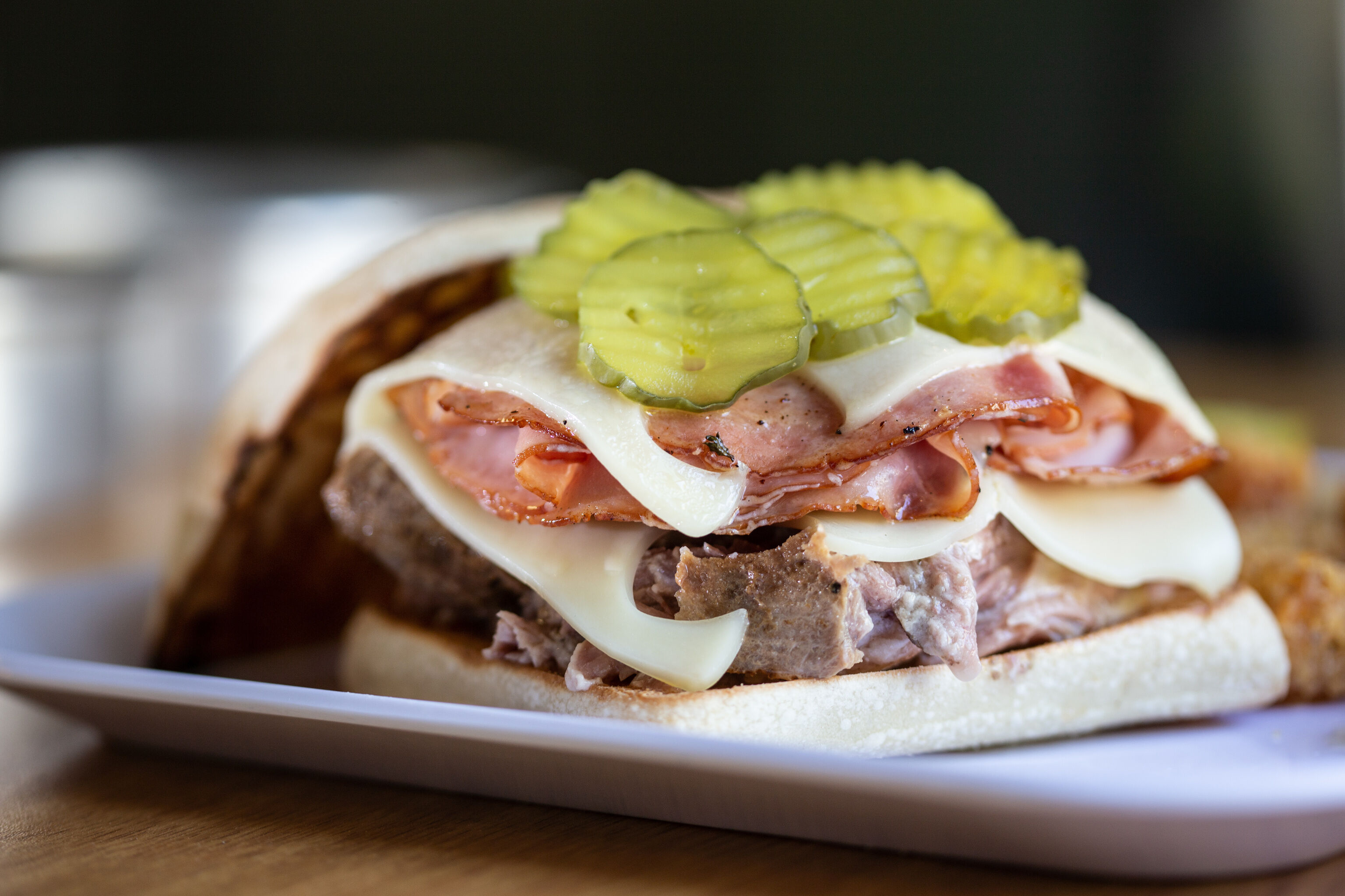 A detailed description of a Cuban Pork Sandwich with pickles, ham, roast pork, and cheese on a soft bread roll.