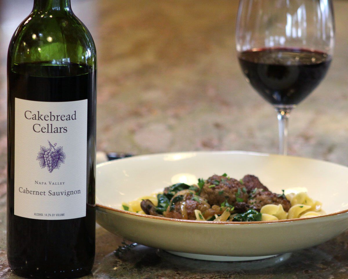 Cakebread Cellars Cabernet Sauvignon wine bottle with Duck Meatballs dish and glass of red wine.