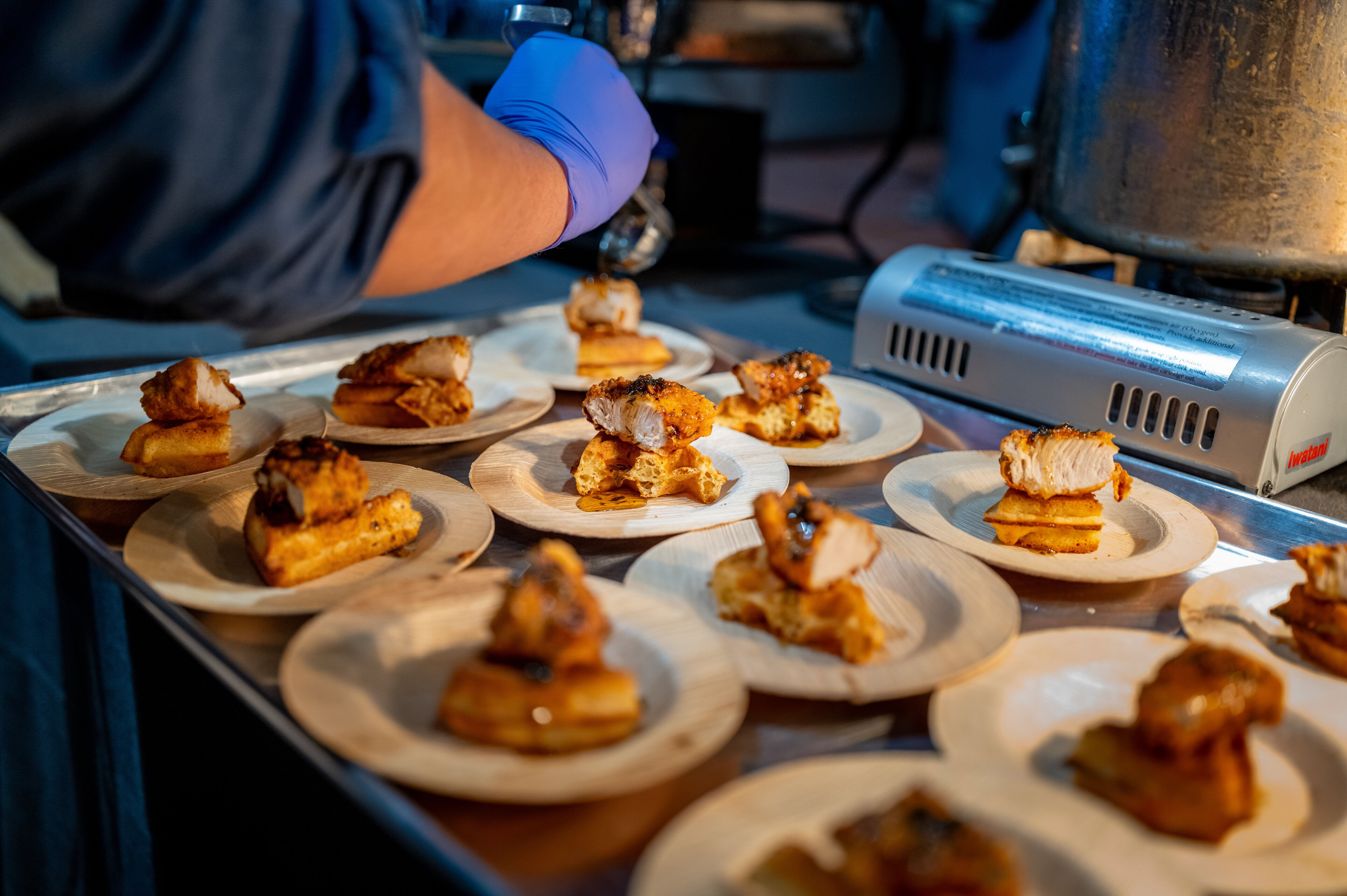 Fried chicken and waffles with brown butter served on small plates at a food event.