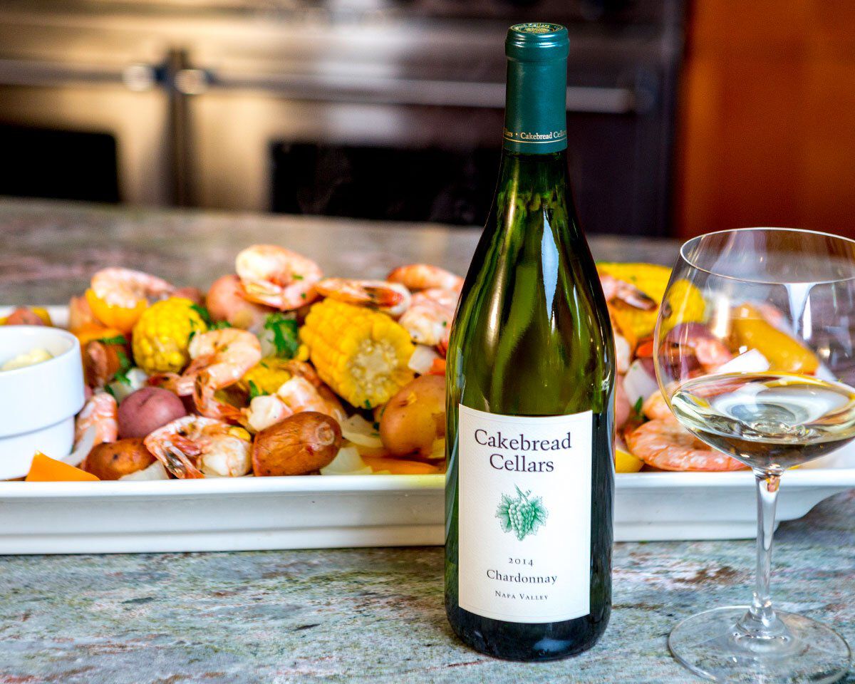 Bottle of Cakebread Cellars Chardonnay with a seafood boil in the background.