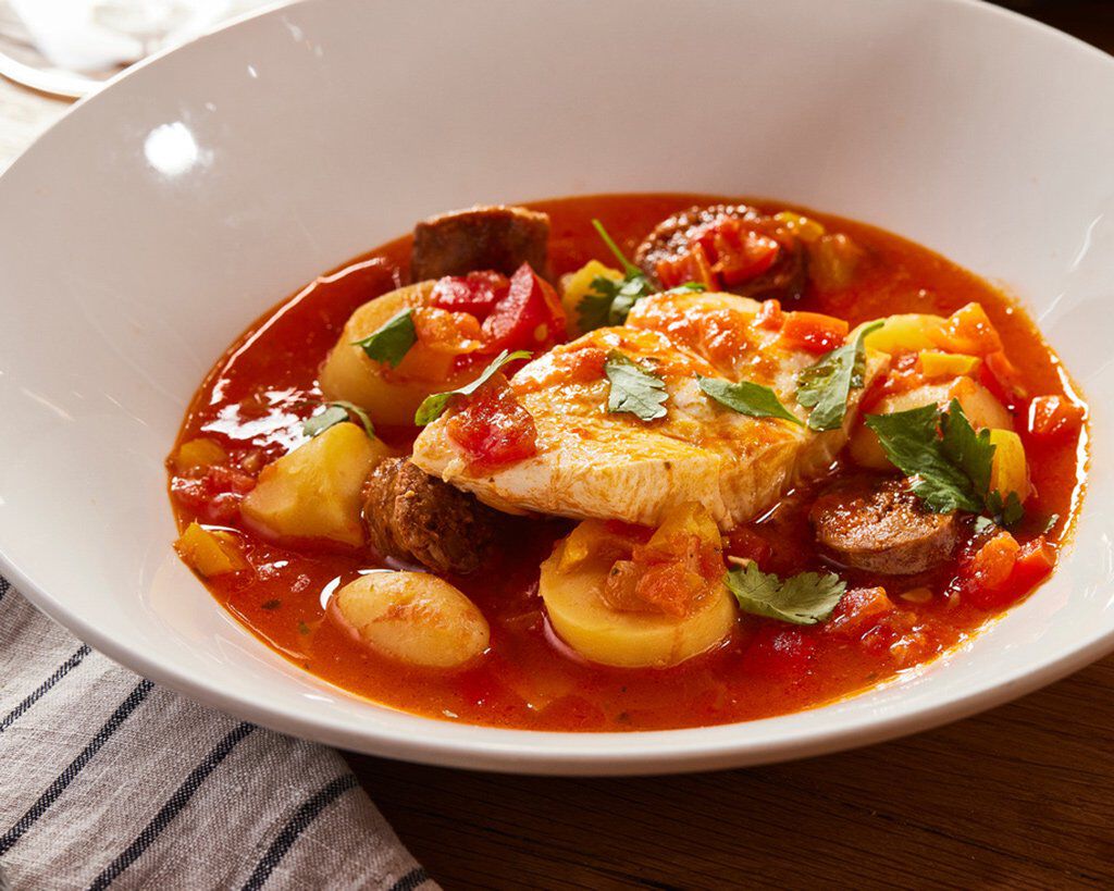 Delicious halibut with chorizo, fingerling potatoes, and spicy tomato broth in a white bowl.