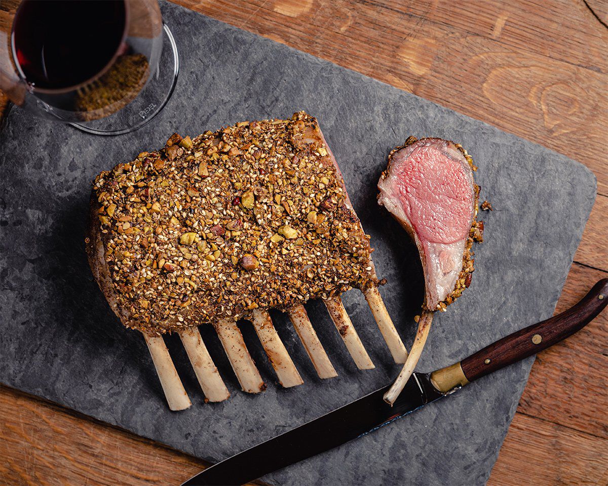 Seared rack of lamb with hazelnut and spice crust on a slate serving board, with a glass of red wine nearby.