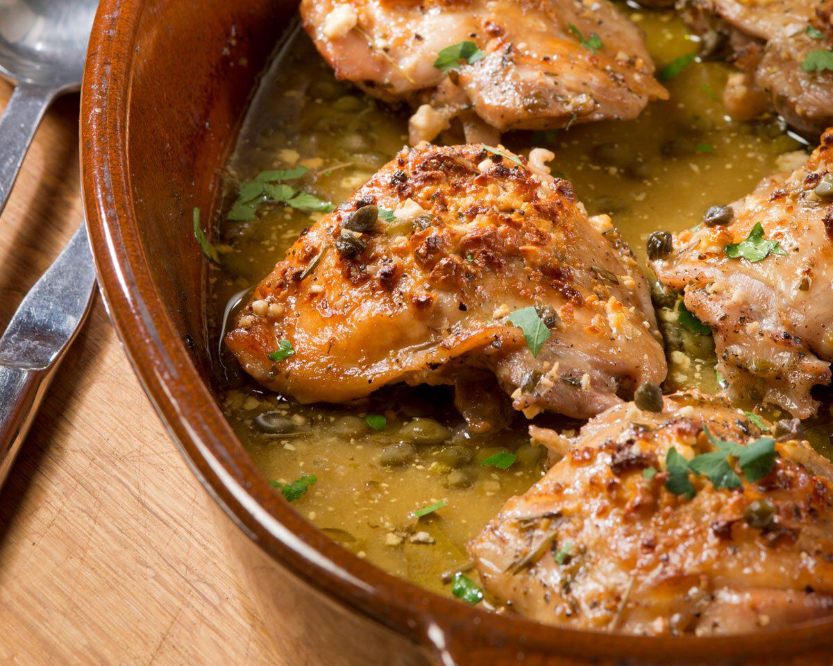 Succulent baked chicken thighs with lemon, feta, and capers in a flavorful sauce, served in a rustic ceramic dish. Perfect fo.