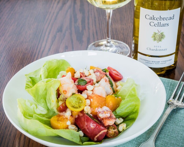 Fresh lobster, tomato, and corn salad served on a bed of lettuce with colorful cherry tomatoes, topped with crumbled cheese,.