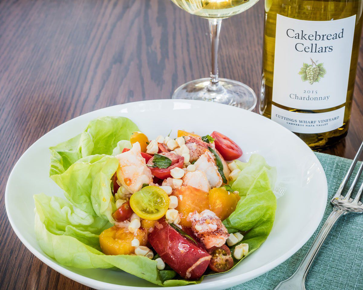 Fresh lobster, tomato, and corn salad served on a bed of lettuce with colorful cherry tomatoes, topped with crumbled cheese,.