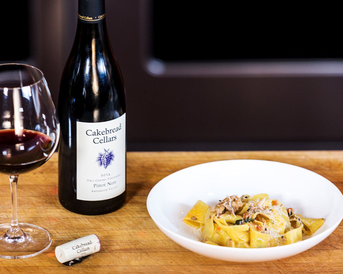 Bottle of Cakebread Cellars Pinot Noir wine with a glass and a plate of pappardelle pasta with duck Bolognese and Tuscan kale.