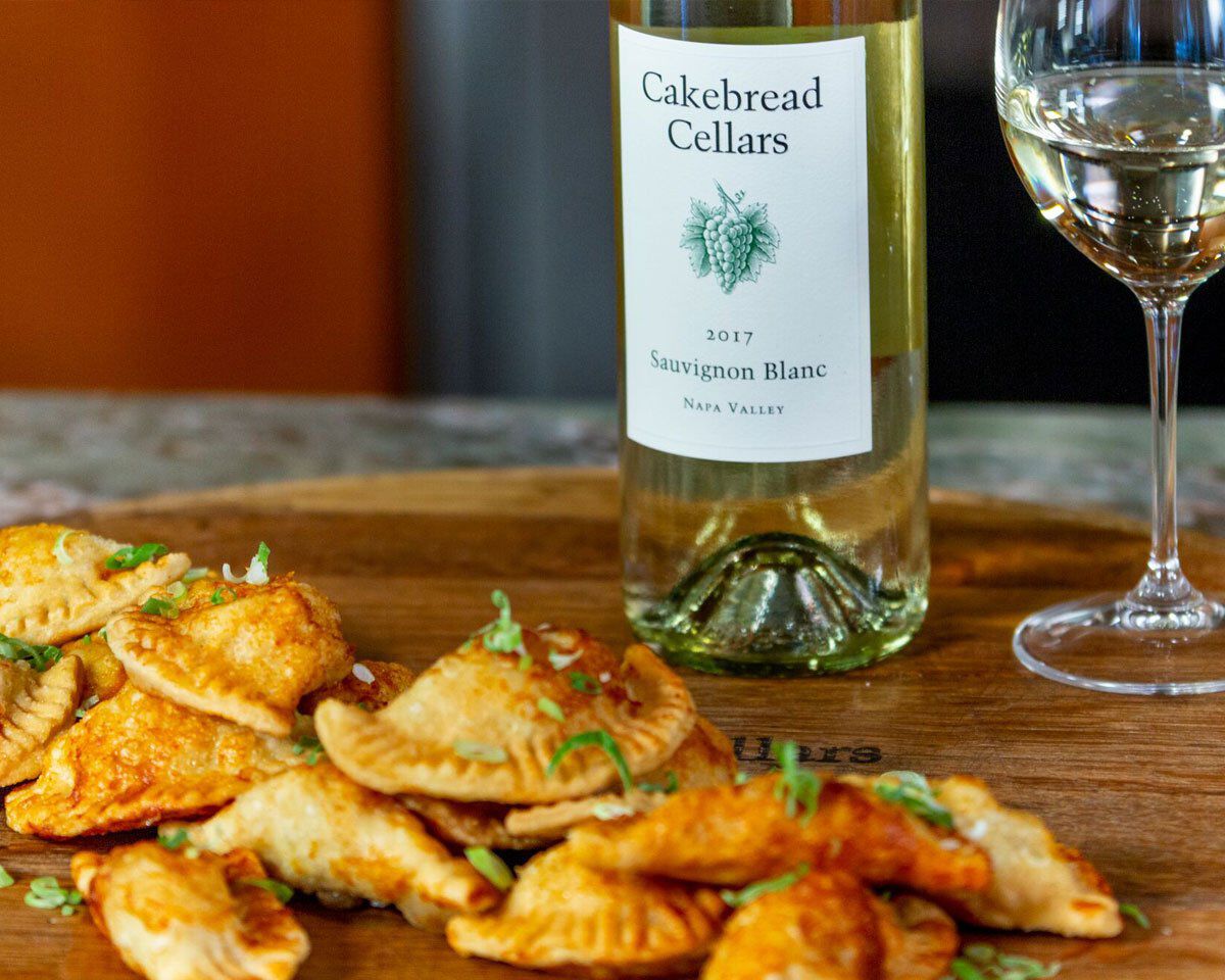 Cakebread Cellars Sauvignon Blanc 2017 wine bottle with a glass of white wine and pierogies with kimchi and potato on a woode.