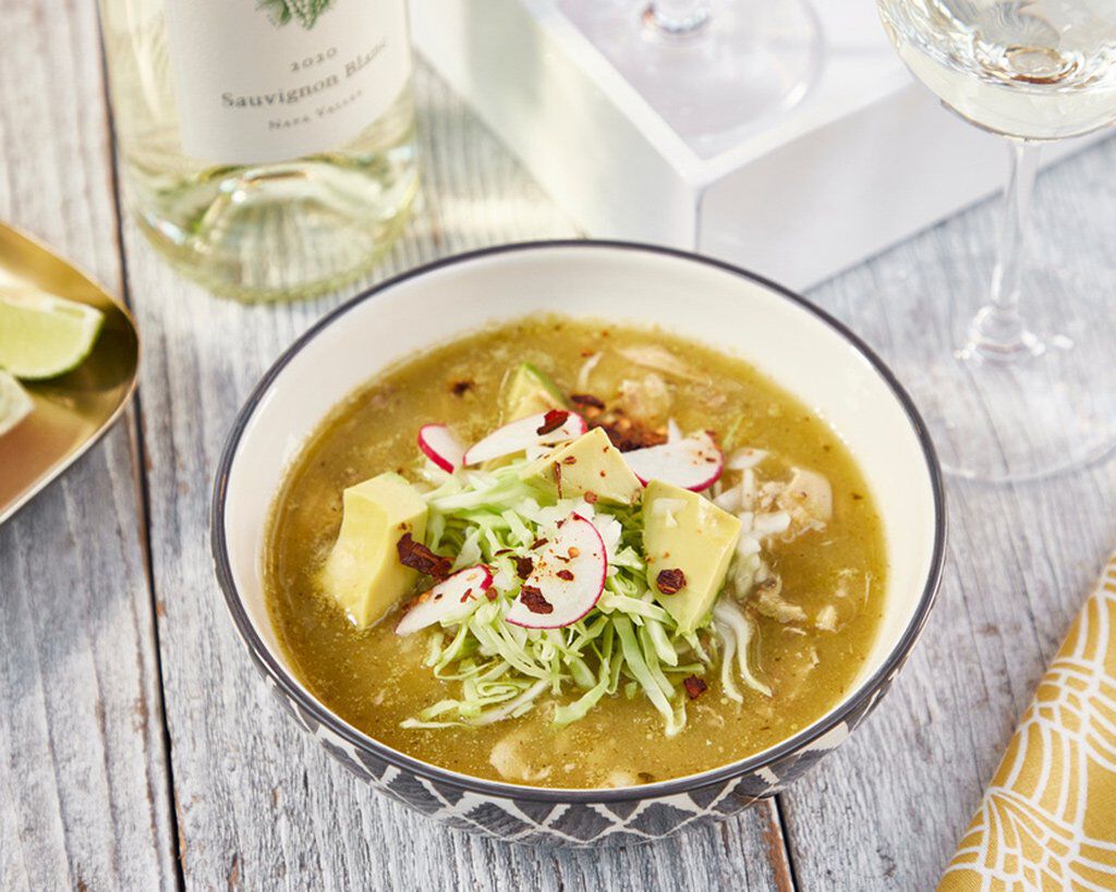 Guacamole with radish and shredded lettuce in a bowl, served with wine and lime, on a rustic wooden table.