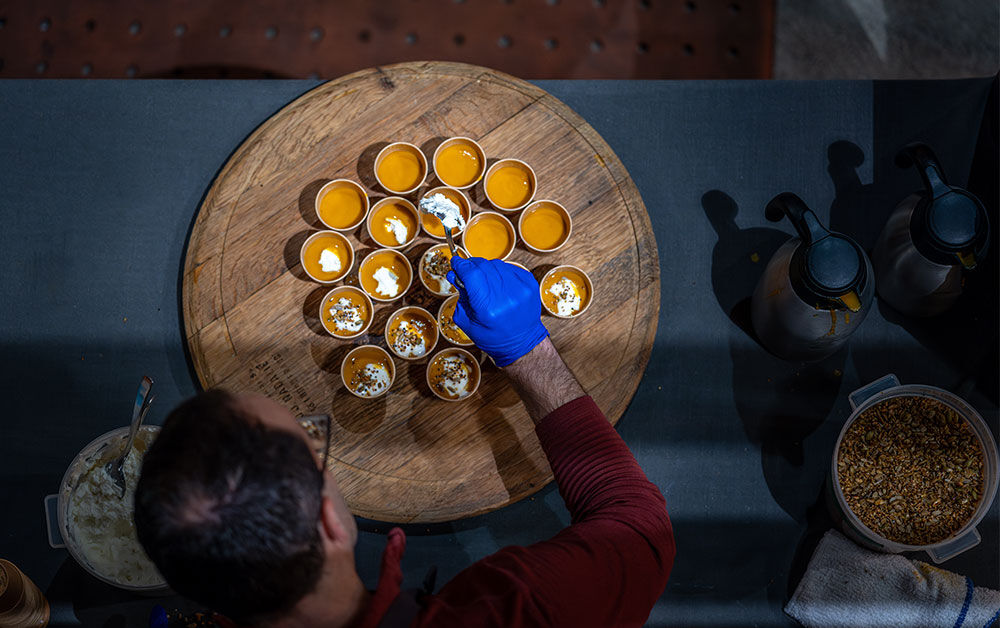 Chef pouring pumpkin chestnut soup into small glasses for serving at a culinary event.