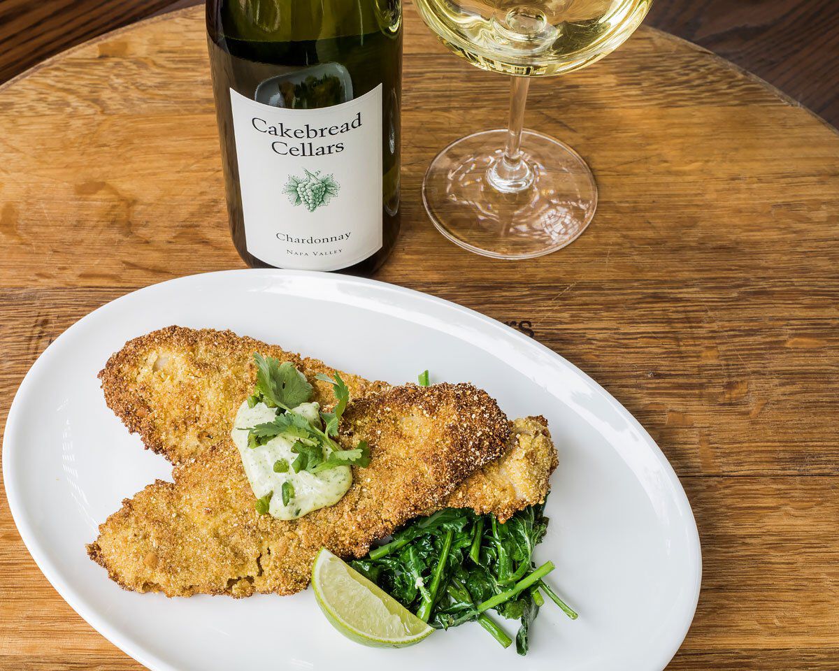 Chardonnay wine, glass of white wine, and a plate of breaded Petrale Sole with greens, lime wedge, and cilantro lime aioli on.