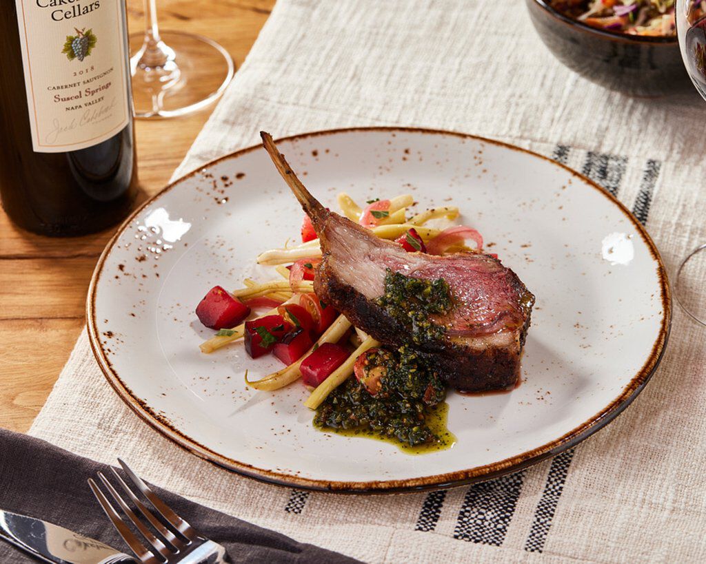 Rack of lamb with pistachio-mint pesto on a rustic plate, served with wine and side salad, perfect for a gourmet dinner.