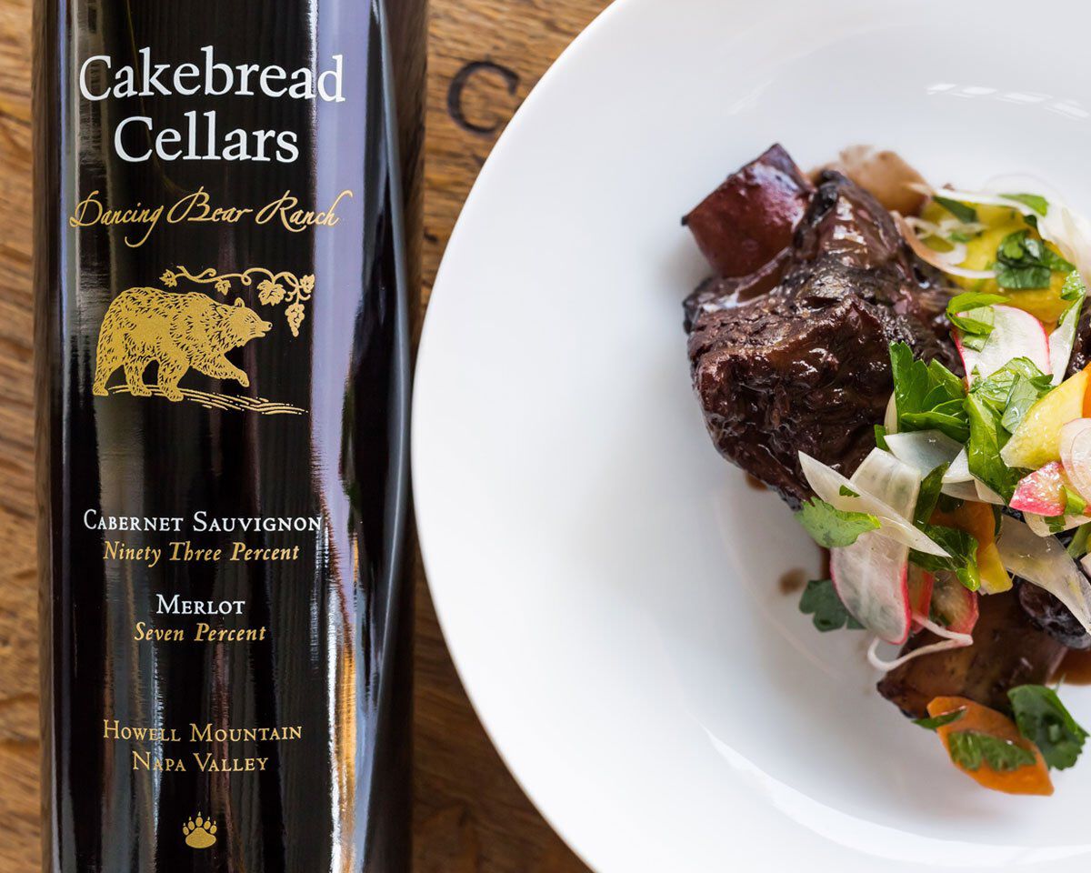 A delicious serving of red wine braised short ribs with shaved vegetable and herb salad on a white plate, paired with Cakebre.