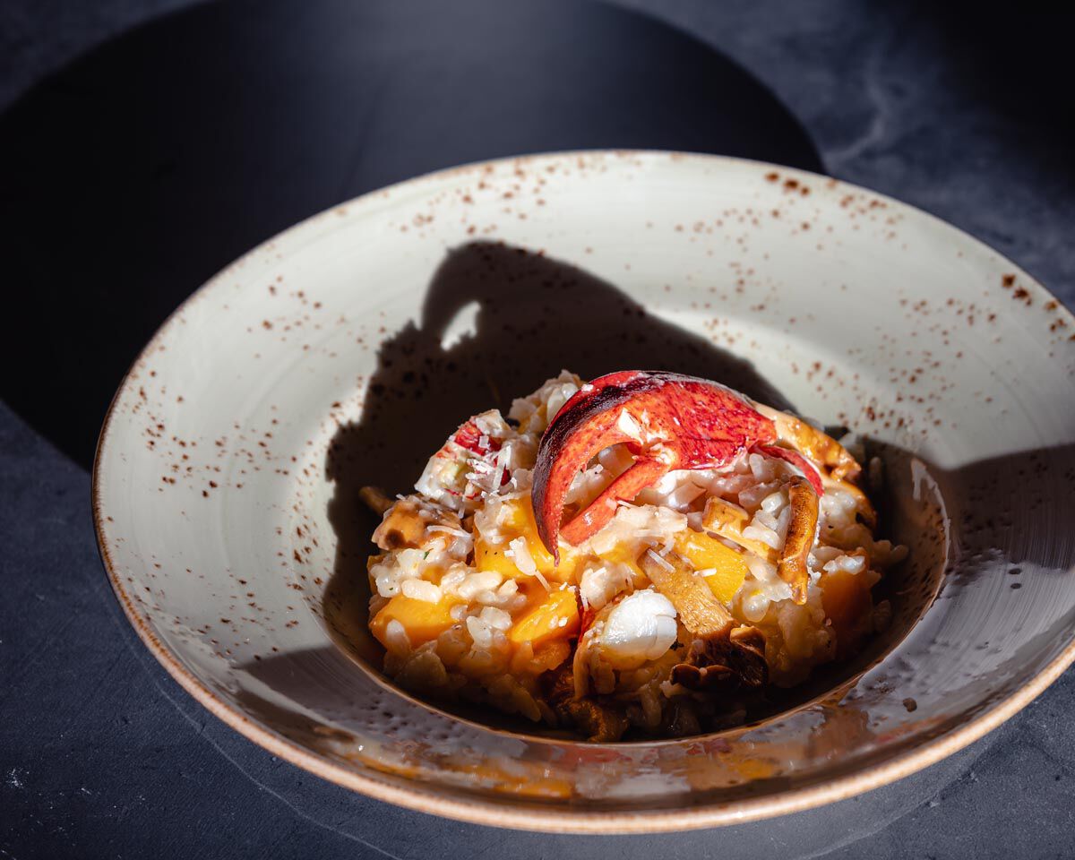 A colorful risotto with lobster, butternut squash, and chanterelle mushrooms served in a white bowl.