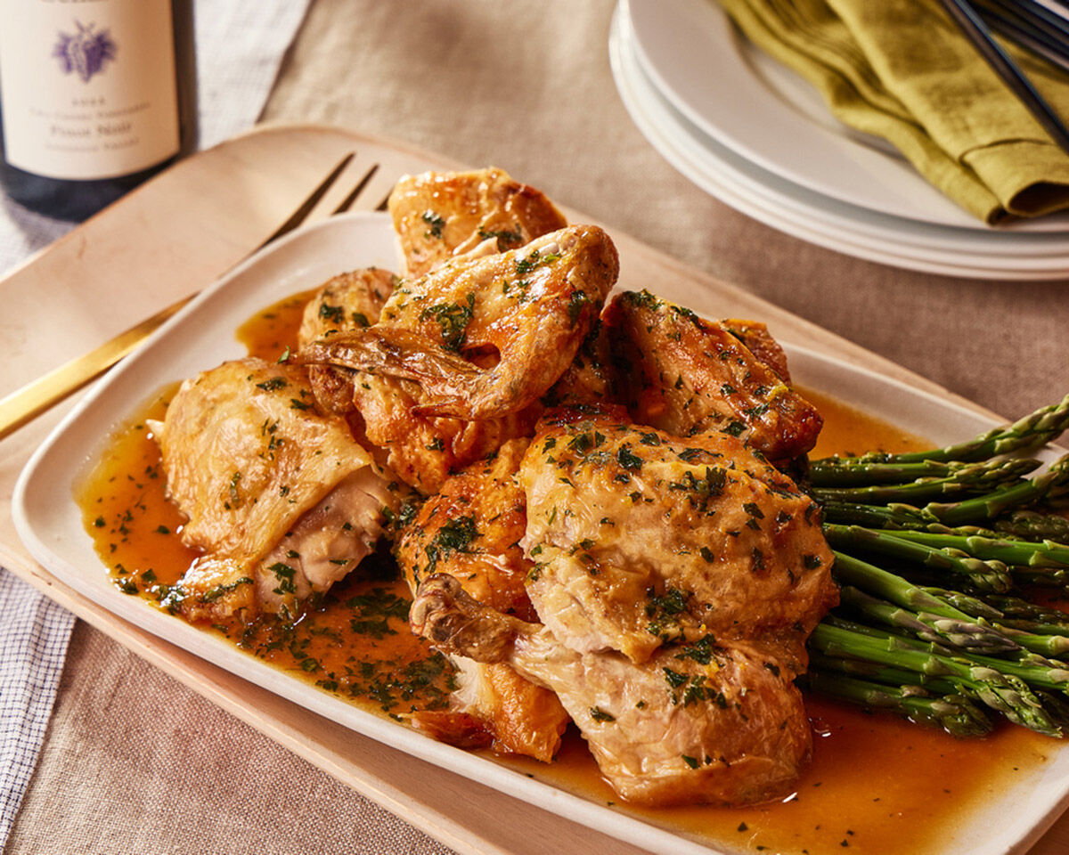 Roast chicken with honey gremolata served with fresh asparagus on a white platter.