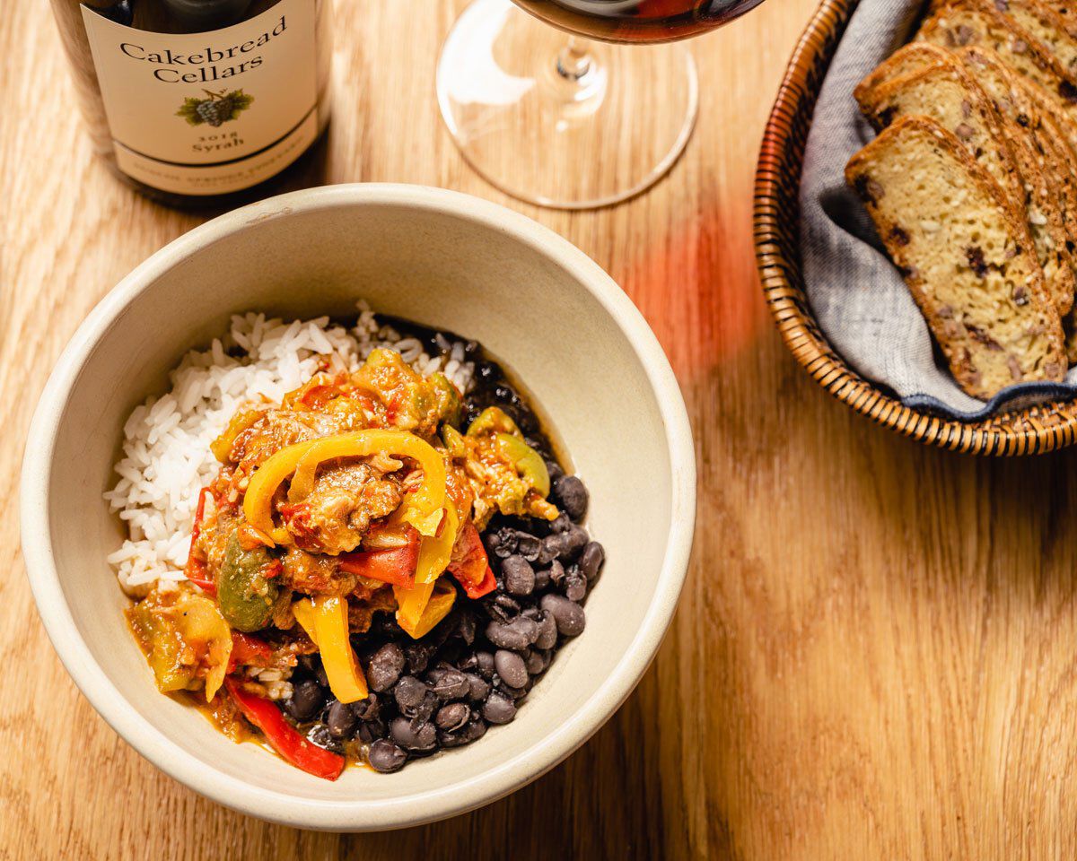 Vegetarian Ropa Vieja with rice, black beans, and colorful peppers served with bread and a glass of red wine.
