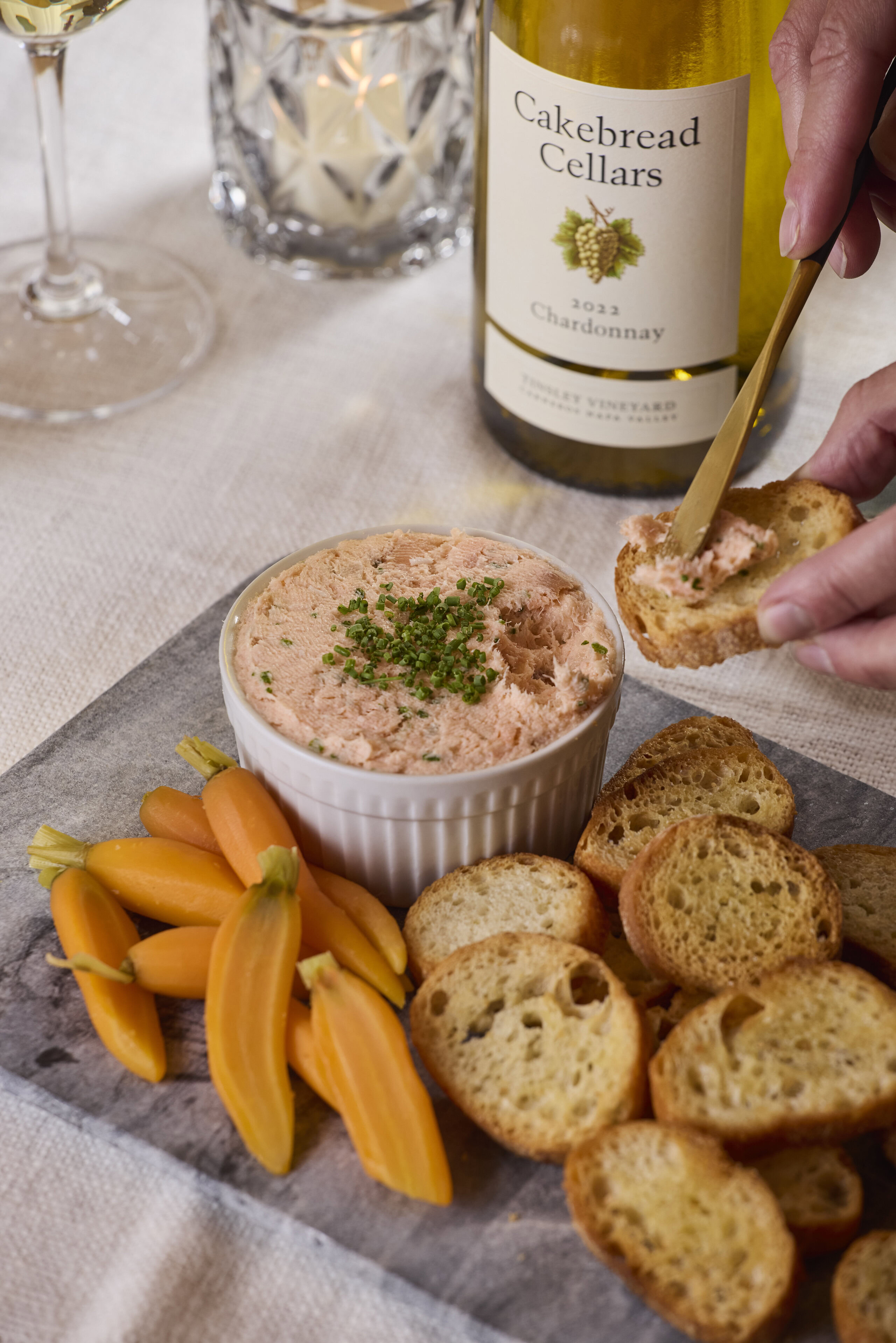 Creamy salmon rillette served with toasted baguette slices and fresh yellow cherry tomatoes, paired with Cakebread Cellars Ch.