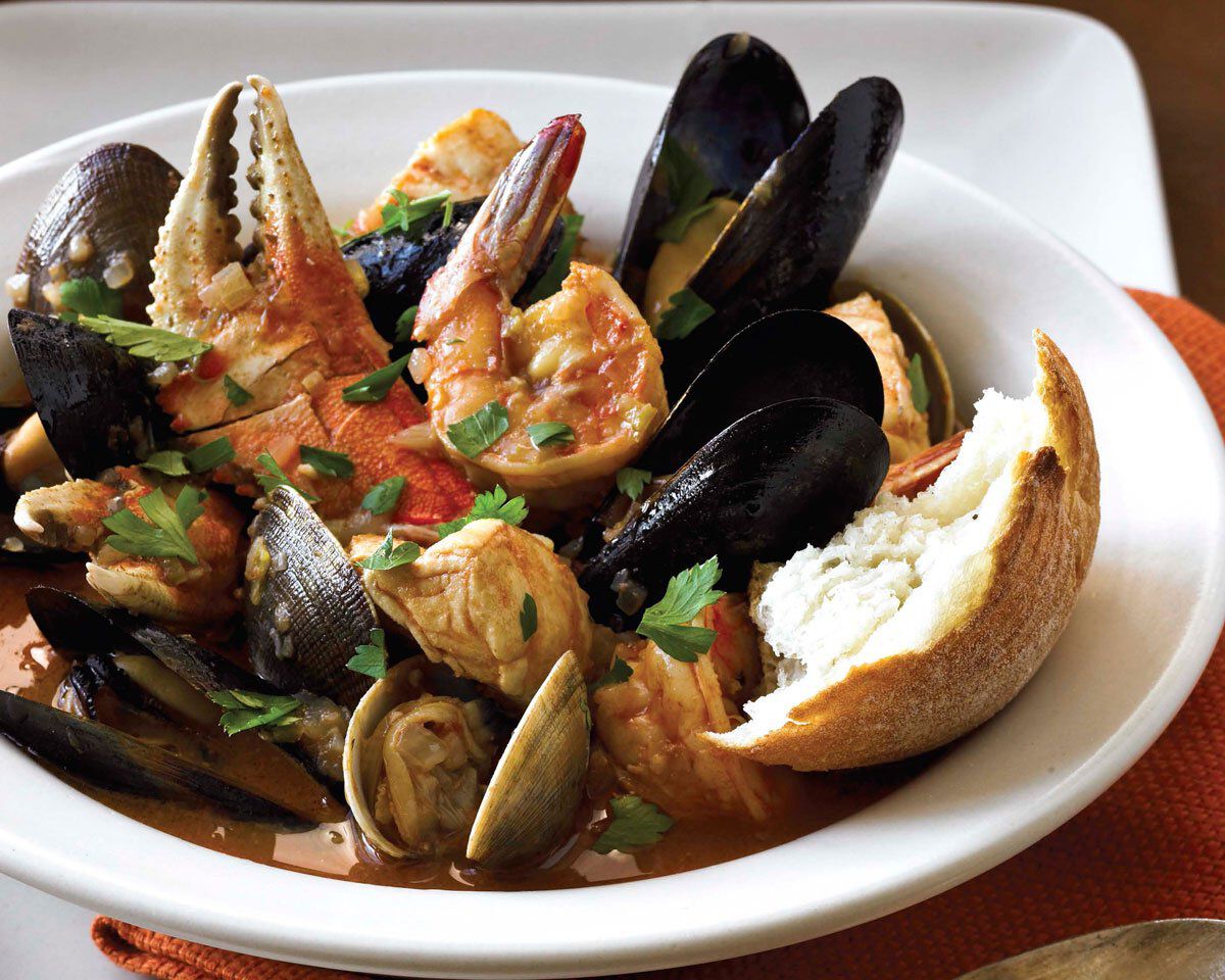 Seafood Cioppino with mussels, shrimp, and crab in a savory tomato broth, served with crusty bread, on a white plate.