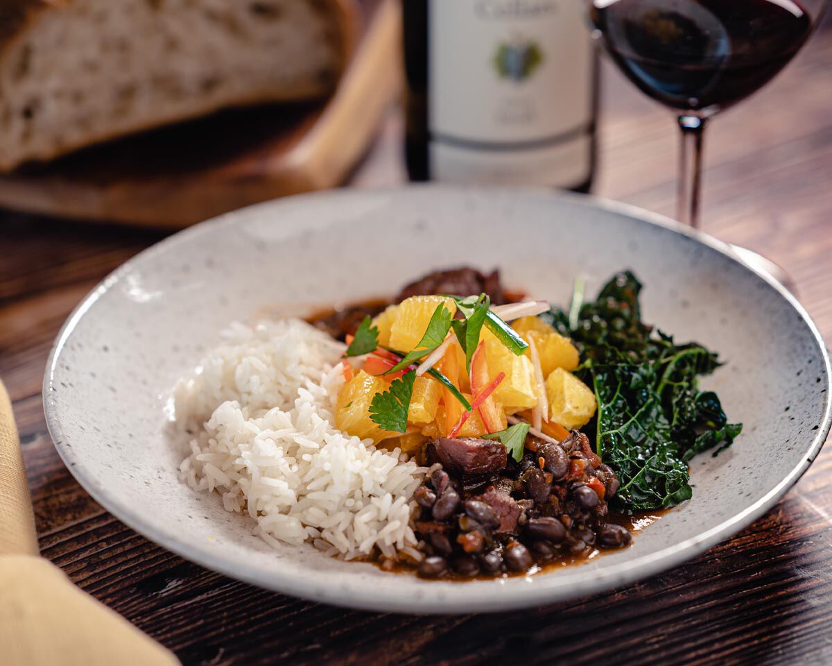 Scott's Brazilian Feijoada with black beans, smoked ham hocks, sausage, kale, and steamed rice on a rustic plate.
