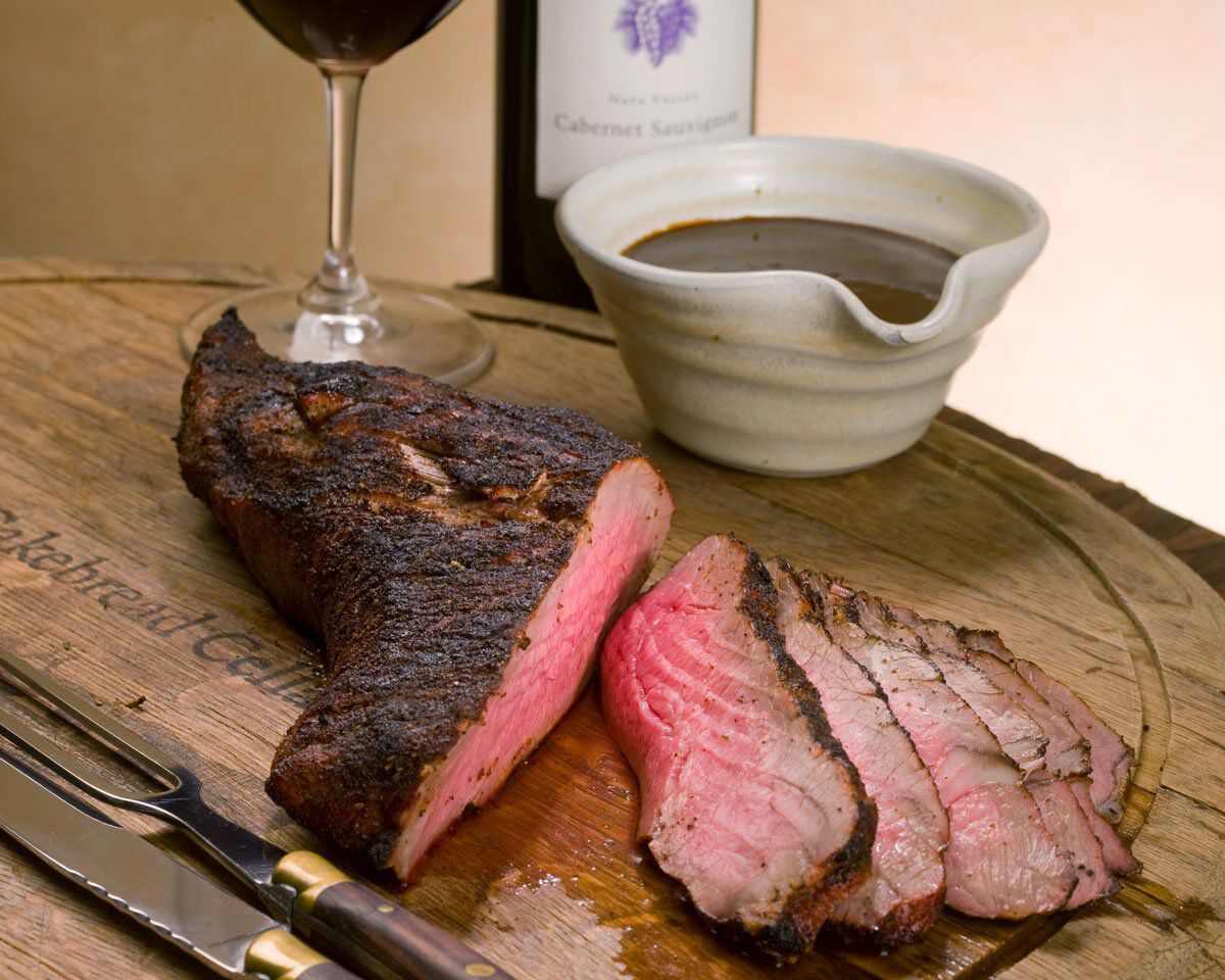 Grilled smoked tri-tip steak with sun-dried cherry steak sauce, served on a wooden cutting board with wine and sauce in the b.