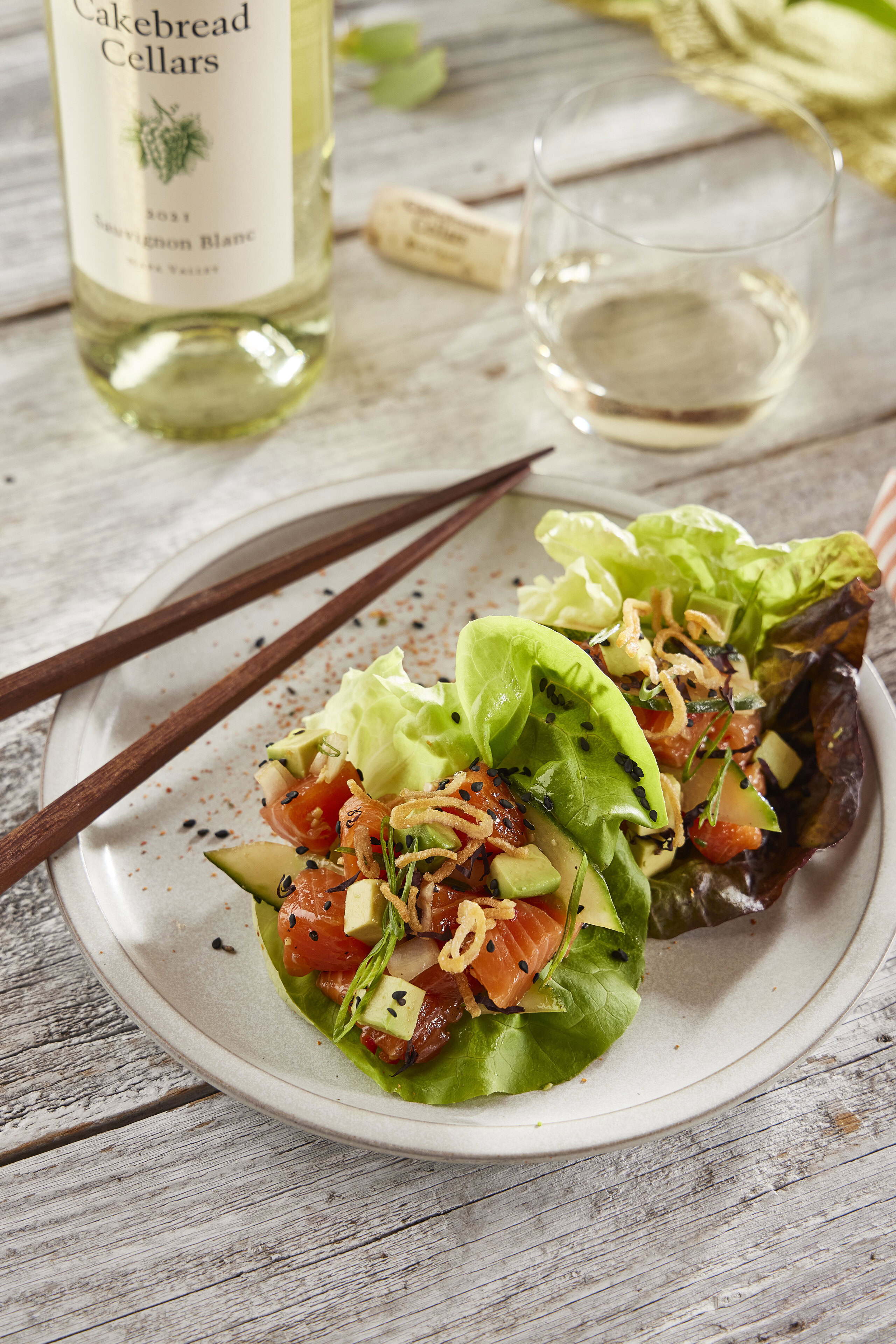 A detailed description of a spicy salmon poke served in lettuce cups, garnished with vegetables and herbs, on a rustic wooden.