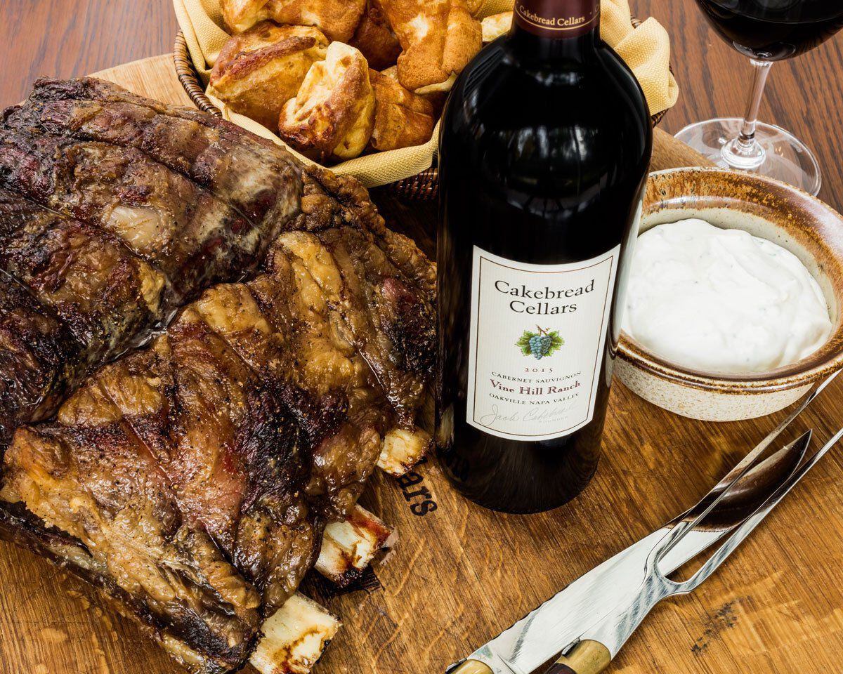 Standing rib roast with horseradish sauce, wine, and roasted potatoes on a wooden table at Cakebread Cellars.