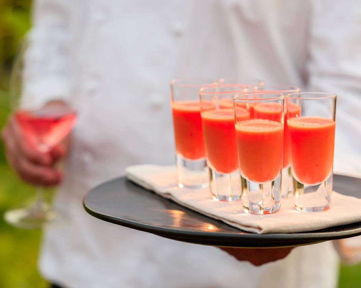 Refreshing watermelon gazpacho served in clear shot glasses on a black tray, perfect for summer tasting and wine pairing.