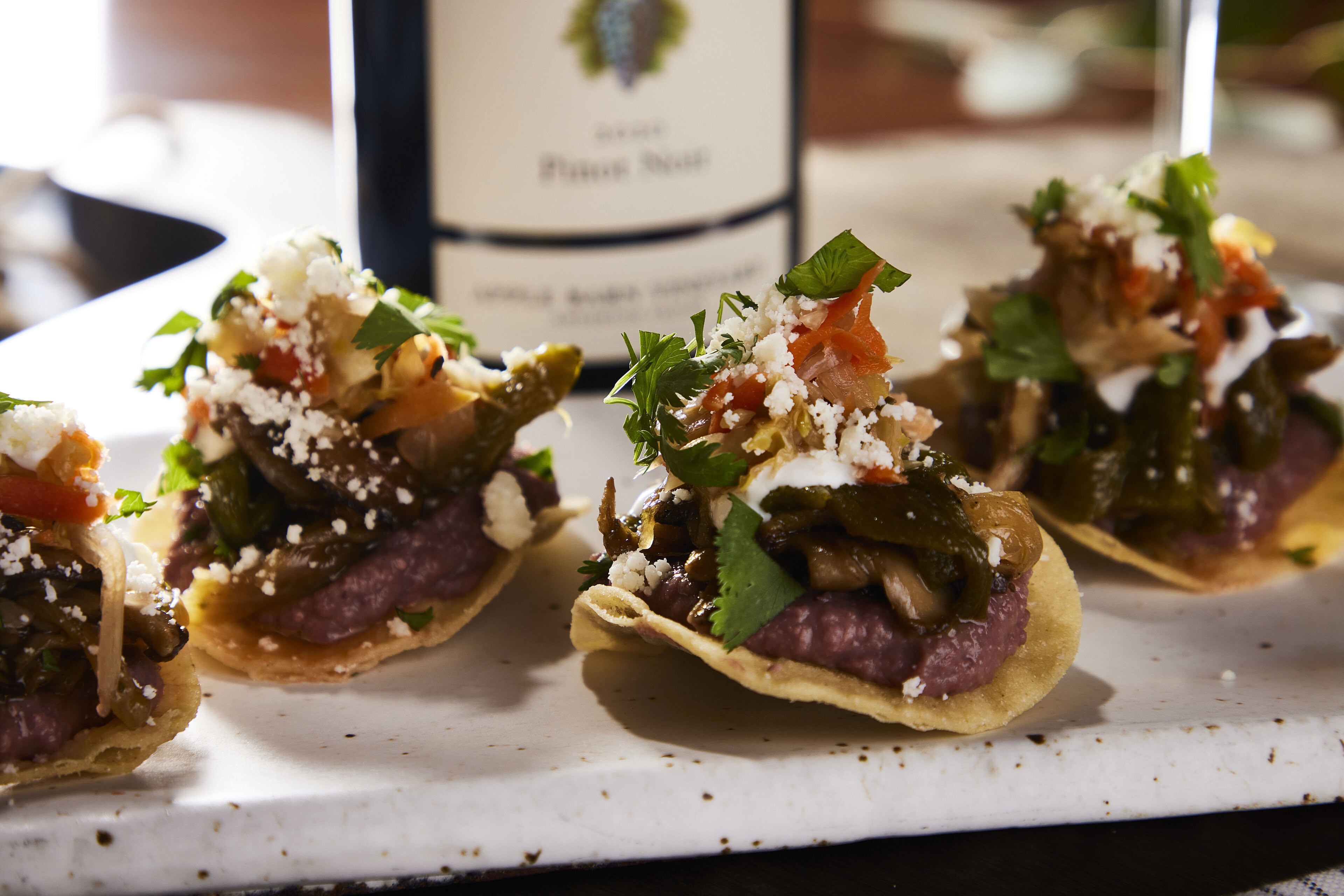 Delicious wild mushroom tostadas topped with lime crema, queso seco, and fresh cilantro on a white serving platter.