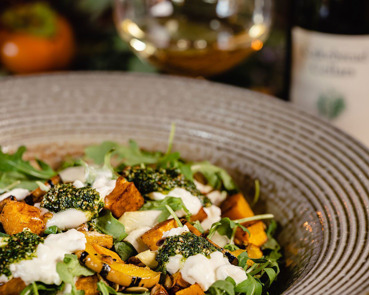 Winter squash salad with burrata cheese, pumpkin seed pesto, and fresh greens in a rustic bowl, perfect for seasonal vegetari.
