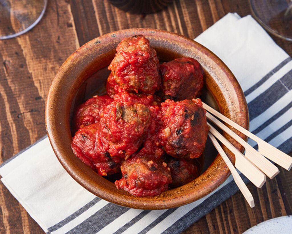 Beef meatballs in tomato sauce served in a rustic bowl on a wooden table with skewers.