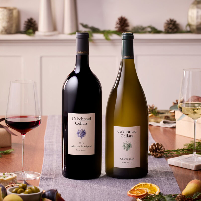 A1: Two bottles of Cakebread Cellars wine, Cabernet Sauvignon and Chardonnay, on a festive table setting with glasses and hol.