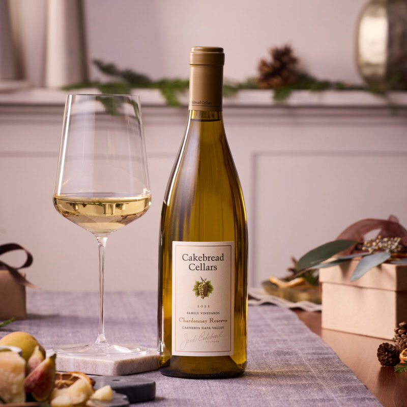 A1: Bottle of Cakebread Cellars Chardonnay wine with a glass of white wine on a table, holiday decorations in the background.