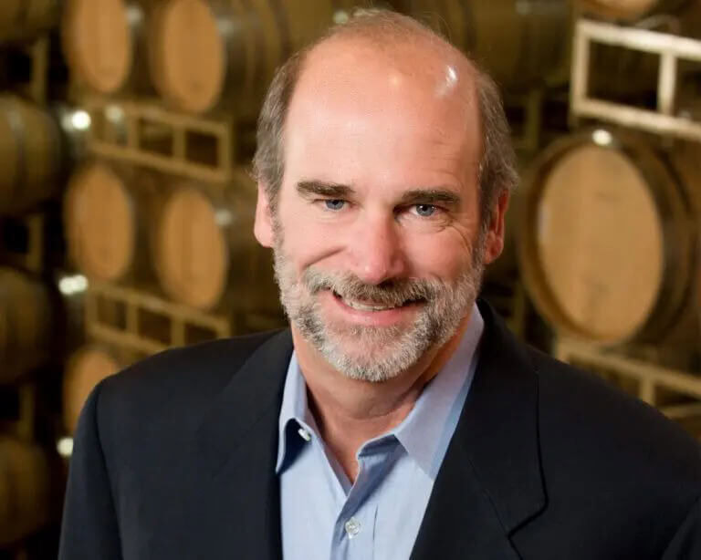 Portrait of Bruce Cakebread in a winery cellar with wine barrels, representing Cakebread Cellars' winemaking expertise.