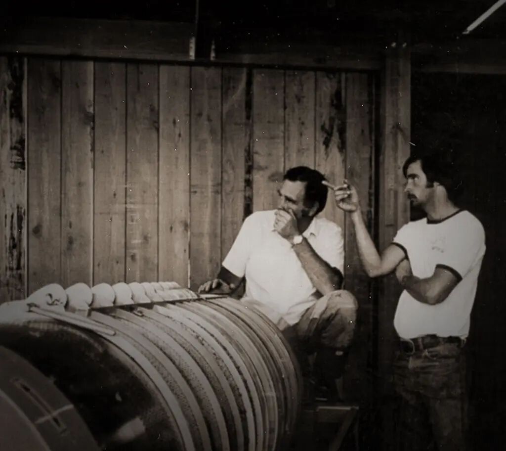 A detailed view of two men inspecting wine barrels in a rustic cellar at Cakebread Cellars.