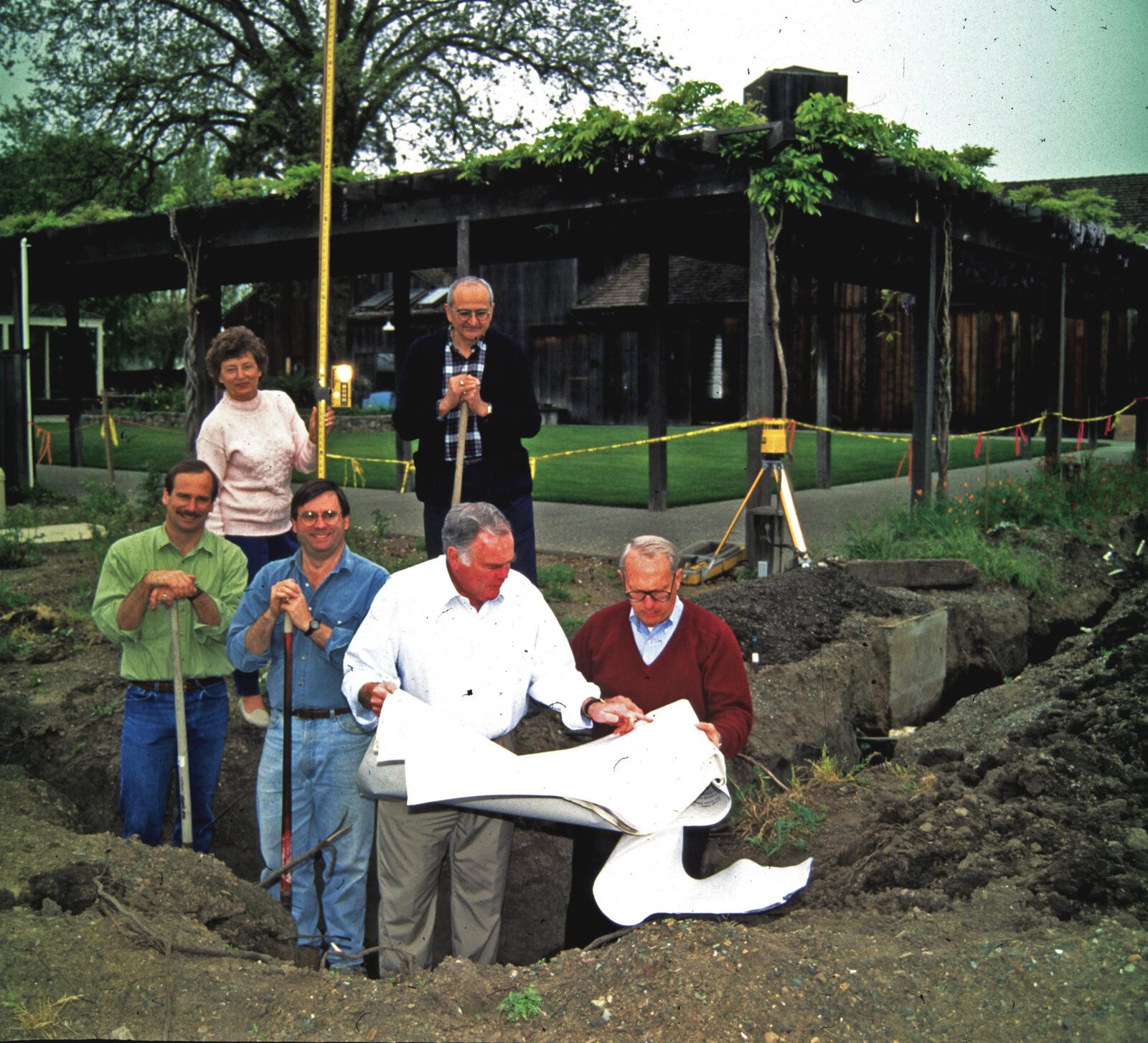 Group of people at a groundbreaking ceremony for a new building, with construction tools and a partially built structure in t.