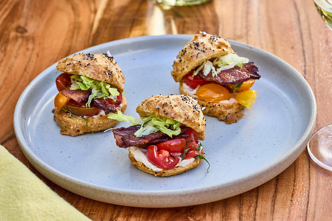 Three gougères filled with bacon, lettuce and tomatoes on a blue plate on a kitchen table.