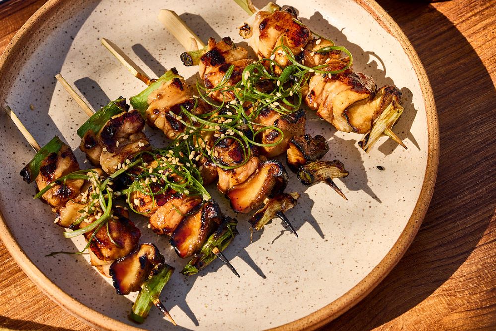 Grilled chickenn yakitori on skewers on a plate sprinkled with green onions and sesame seeds.